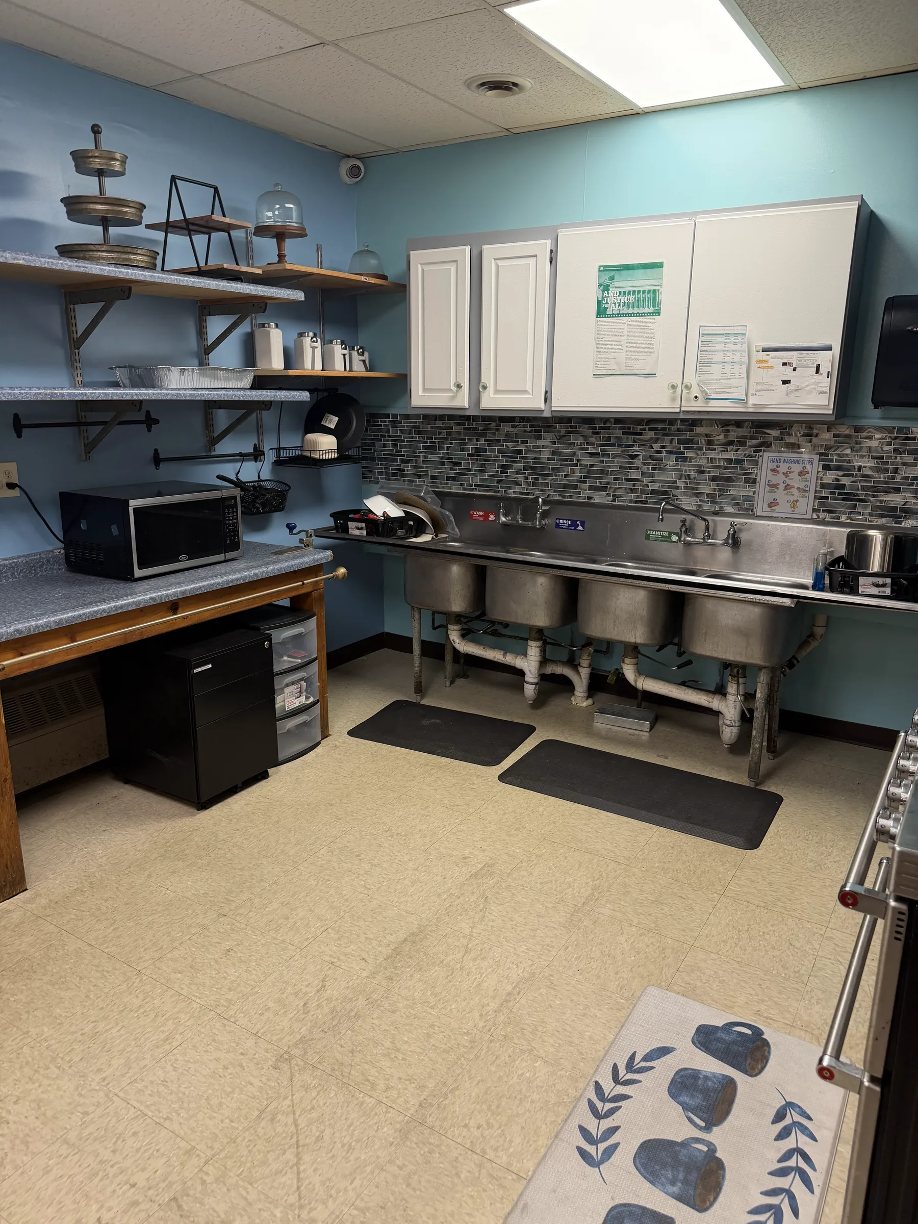 Commercial kitchen with stainless sinks, shelving, and prep space available for rental.